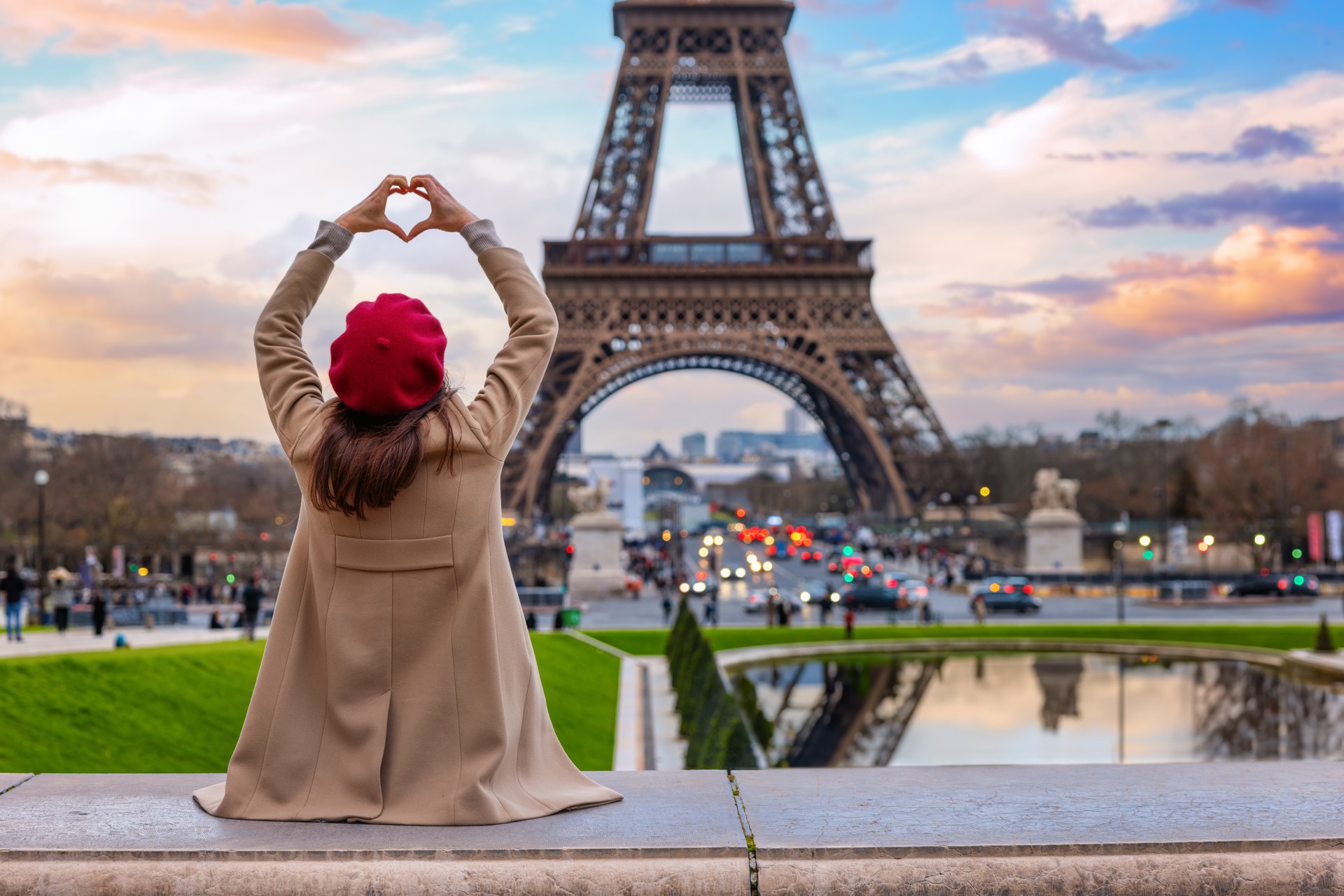 A tourist woman forming a heart with her hands looks at the Eiffel Tower of Paris